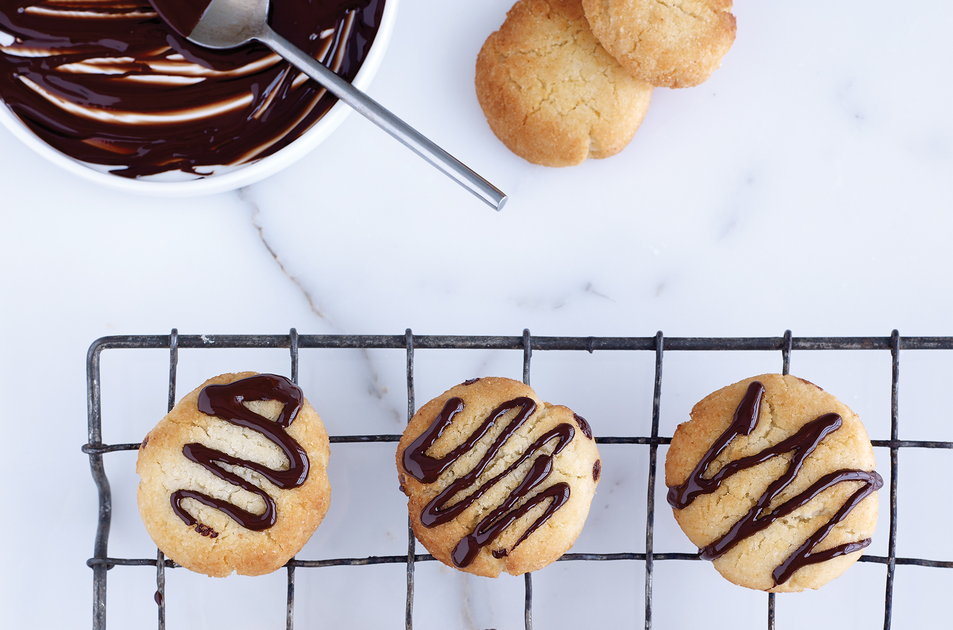 Gluten-Free coconut cookies freshly drizzled with melted chocolate sitting on a wire cooling rack