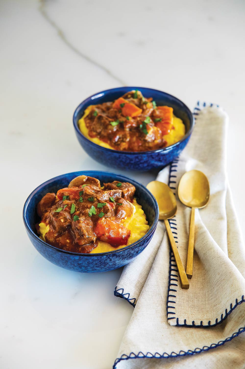 Blue bowls with slow cooker beef stew served on cheesy polenta