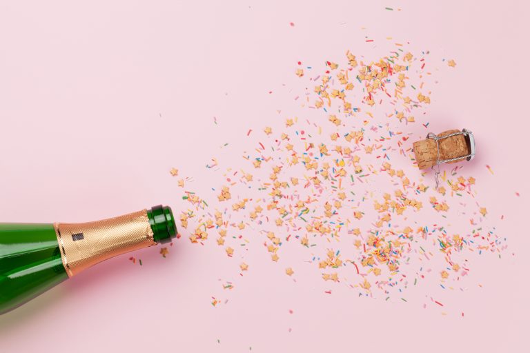 Here's Cheers - gluten-free alcohol guide champagne bottle popping with confetti on pink background