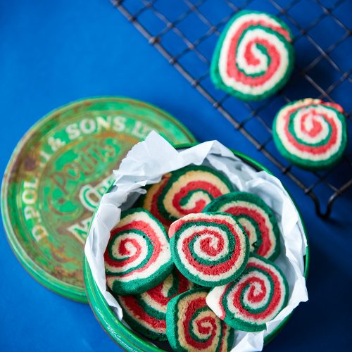 Green-white-red-gluten-free-christmas-pinwhells-in-biscuit-tin-on-blue-background.