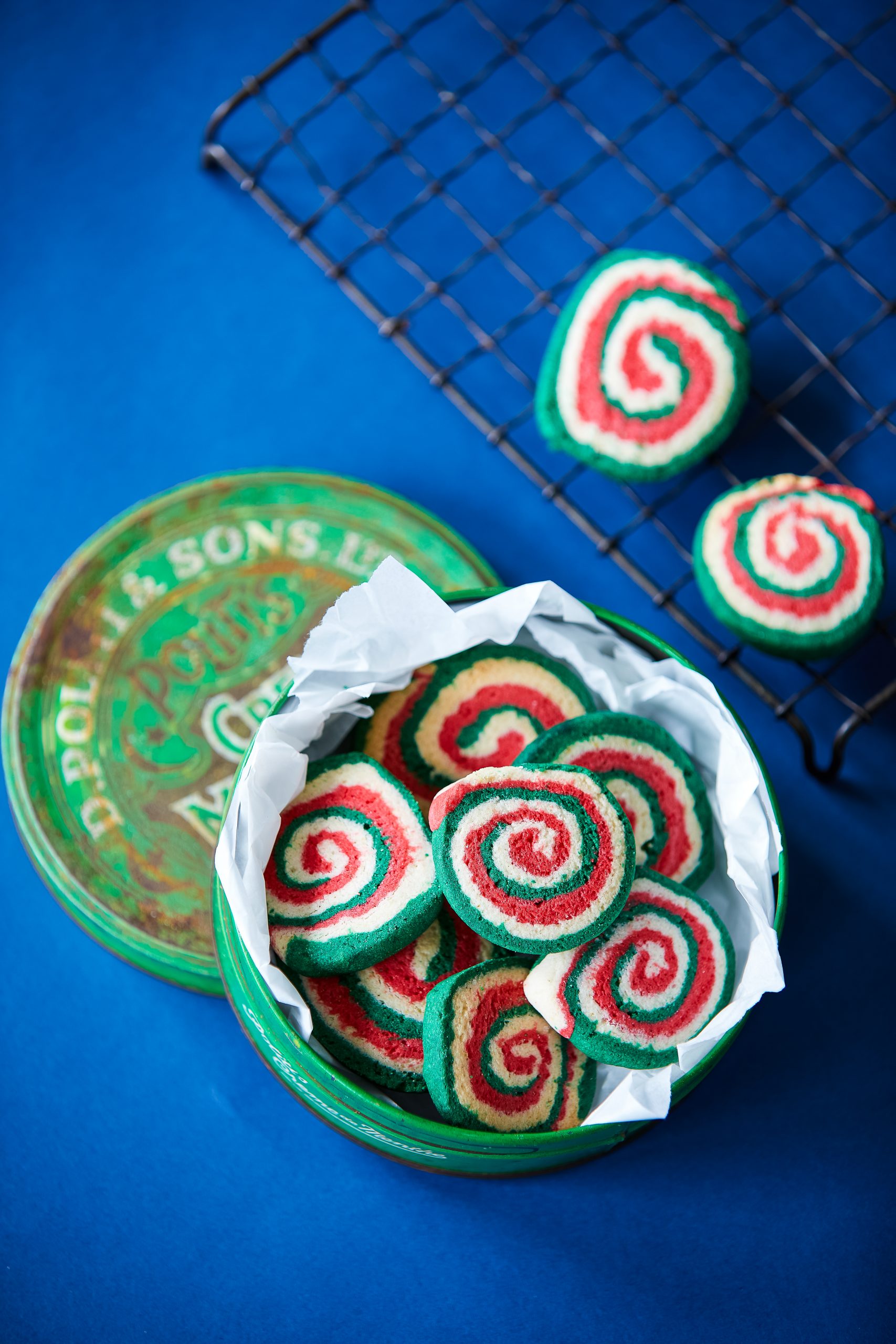 Green-white-red-gluten-free-christmas-pinwhells-in-biscuit-tin-on-blue-background.