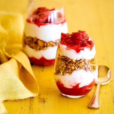 gluten-free breakfast parfait with stewed rhubarb in two glasses on a yellow background