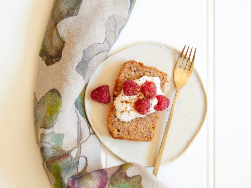 A slice of gluten-free chai banana bread on a plate with a dollop of coconut yoghurt and fresh raspberries.