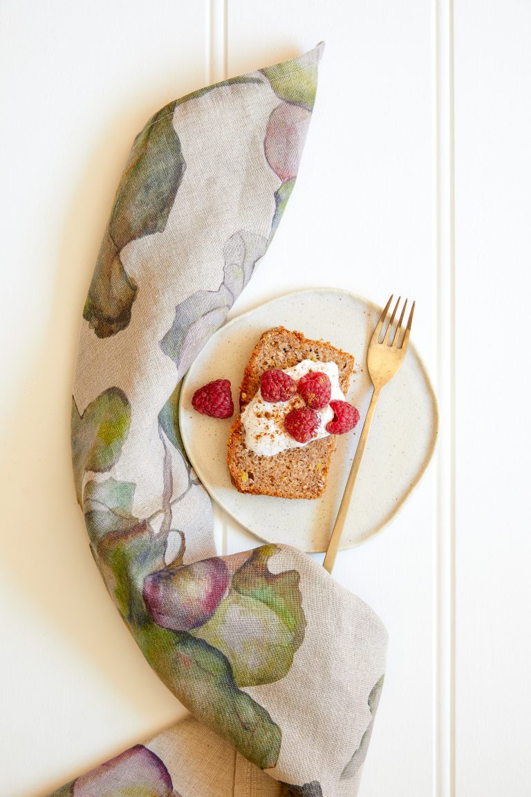 A slice of gluten-free chai banana bread on a plate with a dollop of coconut yoghurt and fresh raspberries.
