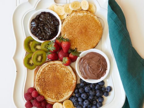 Make ahead gluten-free pancakes on a white platter with assorted fresh fruit, jams and nutella