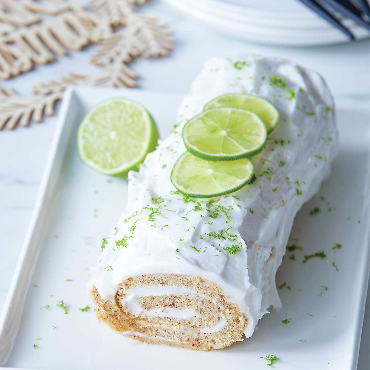 Gluten-free gin and tonic roulade on a white platter with slices of fresh lime and Christmas decorations.