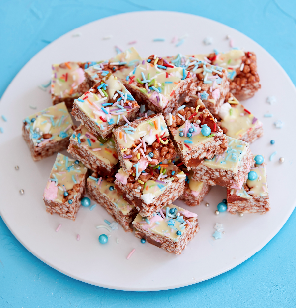 Gluten-free chocolate rainbow bars sliced into squares and arranged on a round white plate on a blue background.