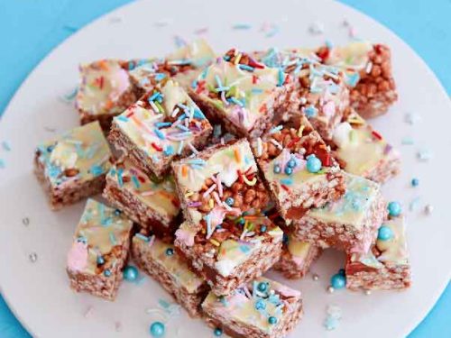 Gluten-free chocolate rainbow bars sliced into squares and arranged on a round white plate on a blue background.
