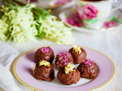 Gluten-Free Violet Crumble truffles arranged on a pink and gold plate for morning tea. In the background are two cups of tea and yellow flowers.