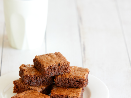 A plate of gluten-free 3-ingredient brownies sliced into squares and arranged on a white plate with a coffee in a white mug in the background.