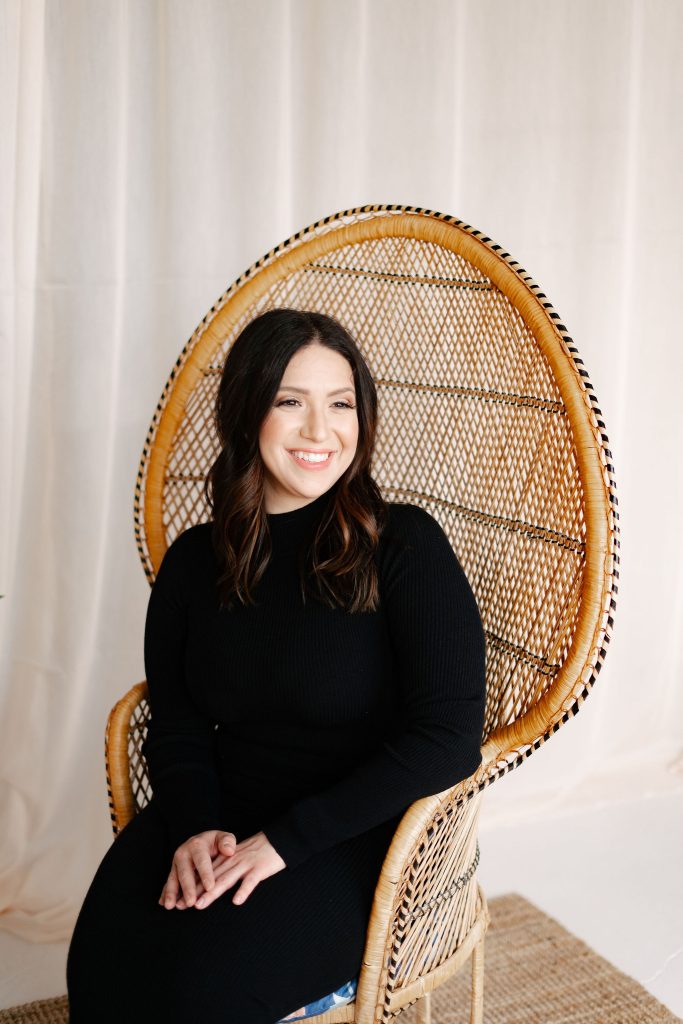 Ashley Gismondi from Toronto (Canada) was diagnosed with coeliac disease in her teens. She is wearing a black turtle-neck jumper and pants and is sitting on a wicker chair.
