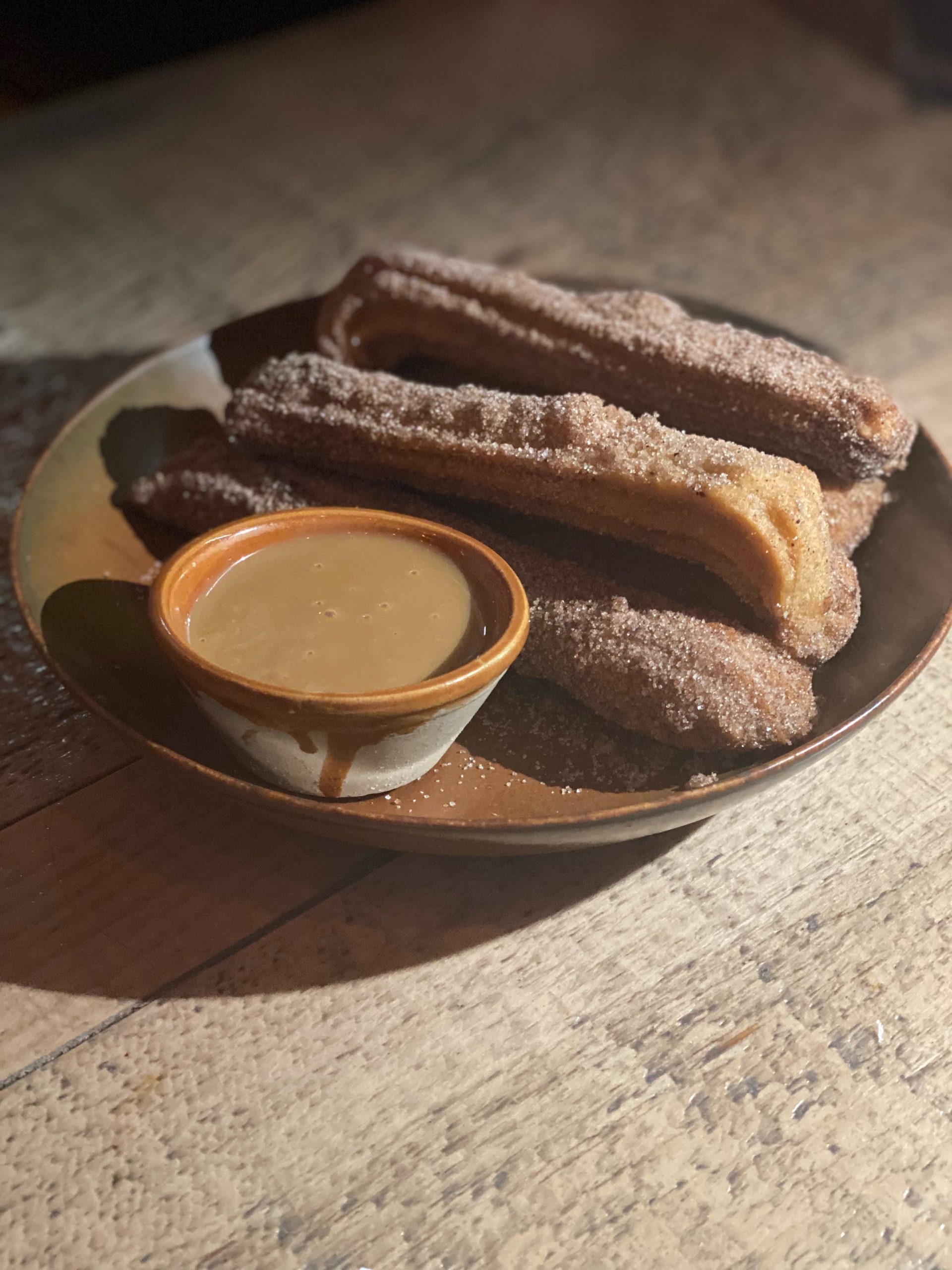 Gluten-free churros on a plate with a dipping sauce.