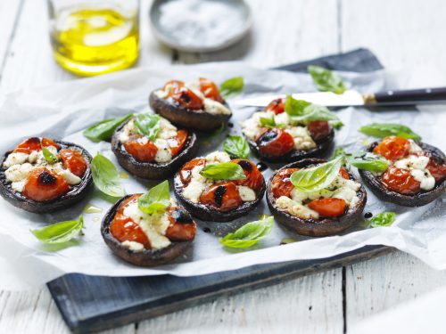 A tray of Portabella mushrooms with pizza topping are arrange on a board sitting on greaseproof paper.