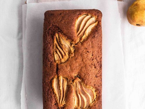 Overhead shot of gluten-free pear loaf with beurre bosc pears sliced and baked into the top. The loaf sits on a piece of greaseproof paper on a wooden chopping board.