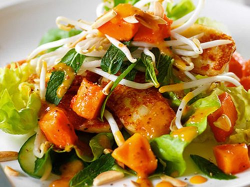Red papaya salad with haloumi is piled high on a round white plate. It's garnishes with bean sprouts and fresh mint leaves.