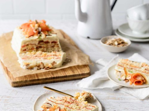 Gluten-free tropical papaya refrigerator cake sits on a wooden board at the back of the image. Two slices are sitting on places at the front of the board. At the back is a vintage enamel coffee pot awithnd cups and sauces.