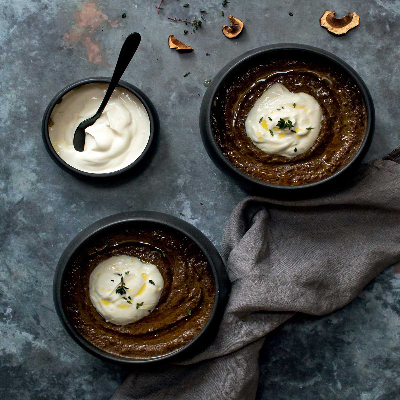 Two dark bowls of creamy wild mushroom soup shot overhead. A smaller bowl is filled with coconut yoghurt. The bowls of soup have a dollop of yoghurt on top.