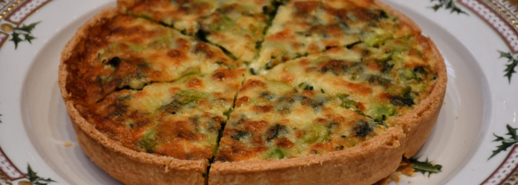 The official photo of the Coronation Quiche from the Royal UK website. A quiche sliced into triangles sites on a round plate.