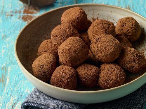 Brown bowl filled with cocoa-coated vegan chocolate truffles. The bowl is resting on a dark blue cloth.