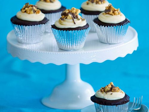 A white cake stand with 5 choc honeycomb cupcakes in silver paper cakes. At the front of the cake stand a single cupcake sits on a small plate with a cake fork.