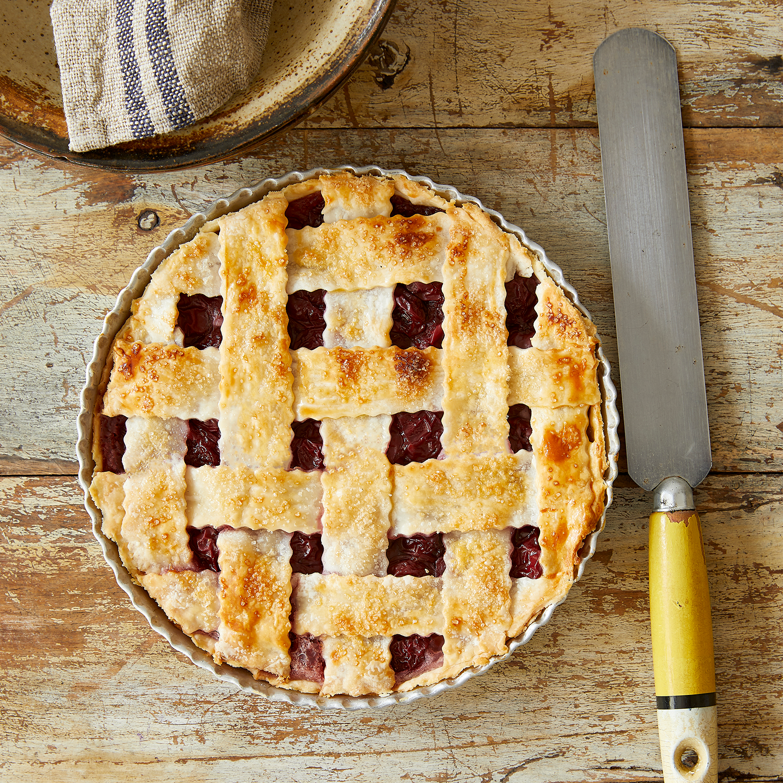 A gluten-free cherry pie on a wooden background. The pie is in a metal pie tin and has a lattice gluten-free pastry top.