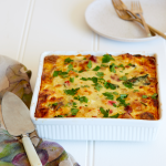 A large white baking dish with gluten-free breakfast strata topped with fresh herbs. A cake lift sits to the side ready to serve onto plates.