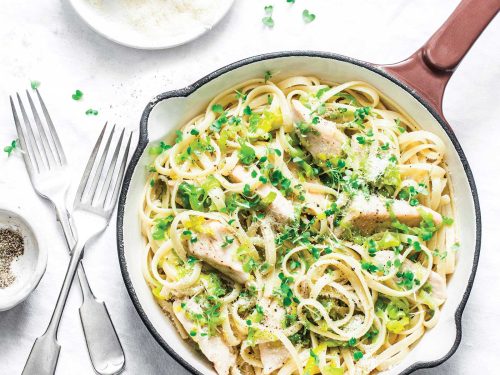 A white saucepan with wooden handle with gluten-free chicken & leek fettucine. The pasta has been garnished with micro herbs and grated Parmesan.