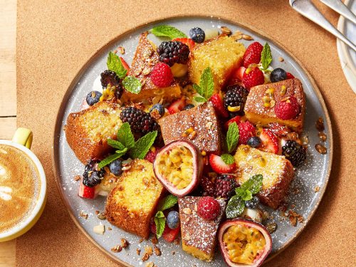 A large round serving platter topped with squares of gluten-free lemon polenta cake, fresh berries, passionfruit halves and mint leaves.
