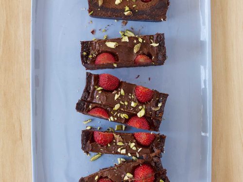 A vegan chocolate tart, sliced into rectangular pieces sitting on a blue platter. The tart is topped with fresh raspberries and crushed pistachio.
