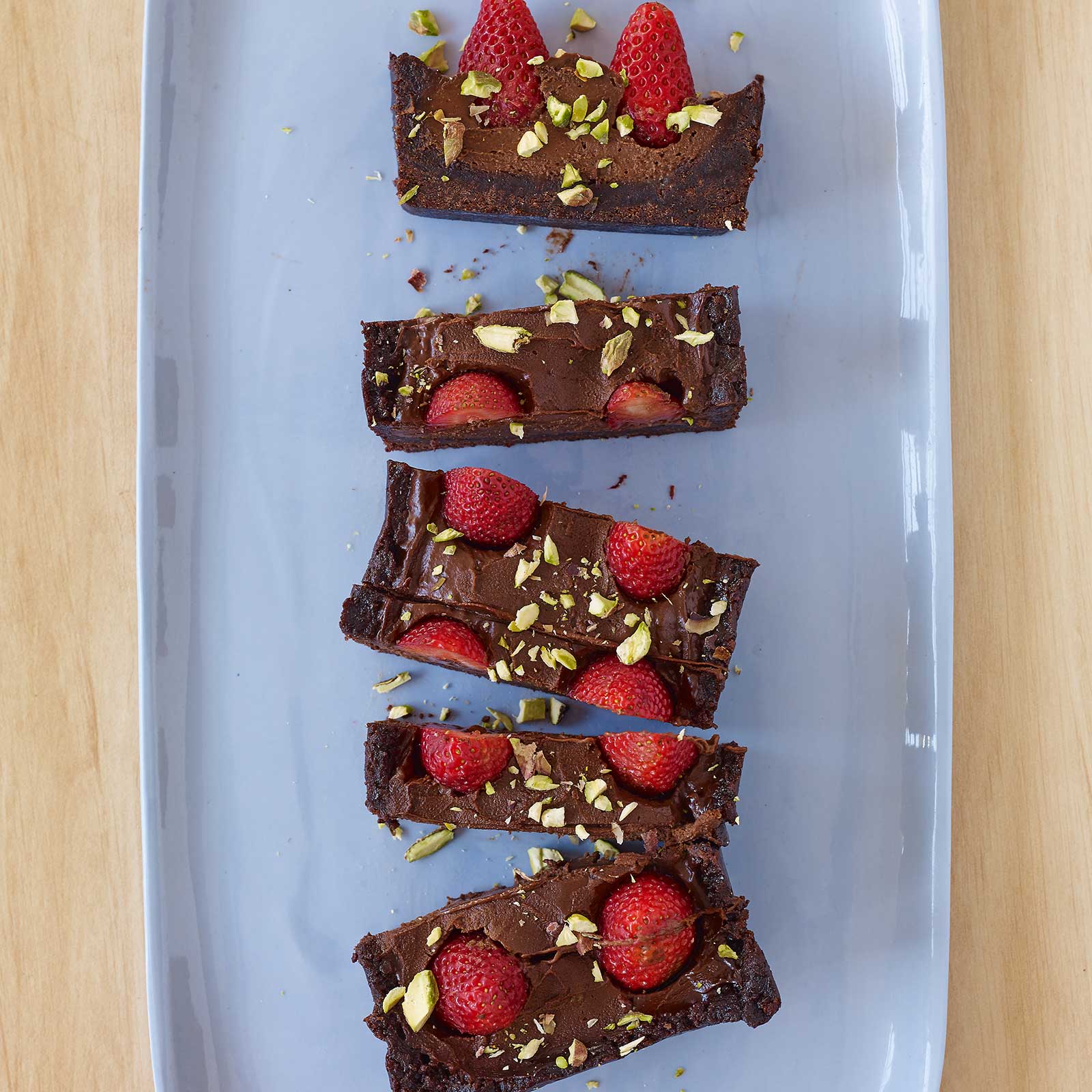 A vegan chocolate tart, sliced into rectangular pieces sitting on a blue platter. The tart is topped with fresh raspberries and crushed pistachio.