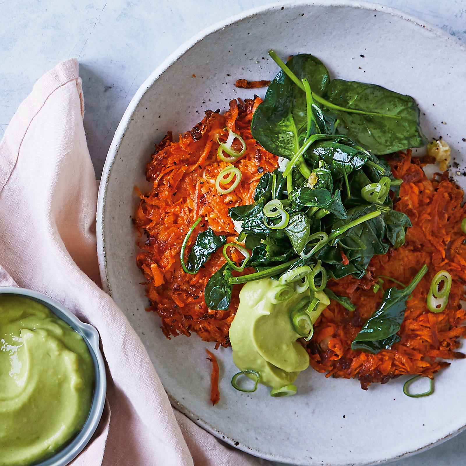Sweet Potato and Halloumi Fritters arranged in a bowl. Topped with sliced spring onion, sauted spinach and a dollop of pureed avocado.