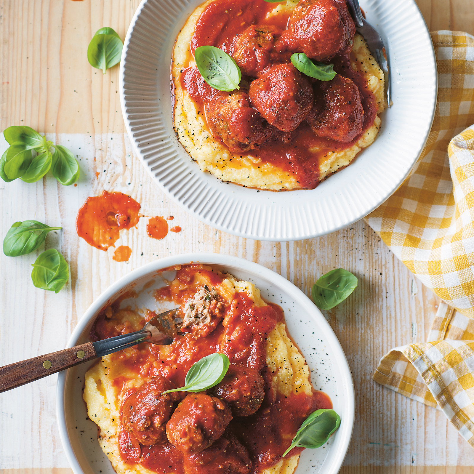 Two bowls of ricotta zucchini meatballs, served over soft polenta. Topped with fresh basil leaves.