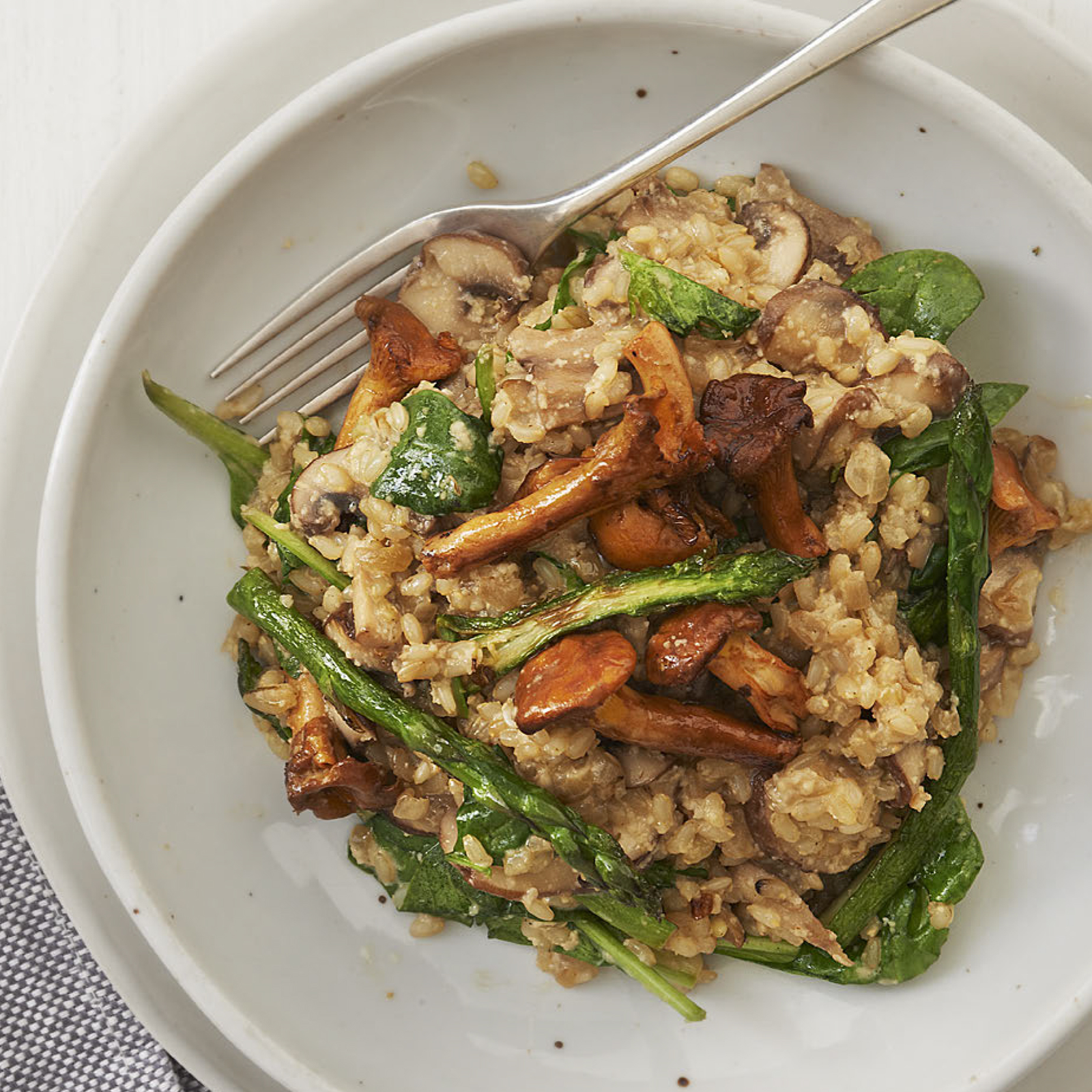 A white bowl of chanterelle mushroom and asparagus risotto with a fork in it ready to be eaten.