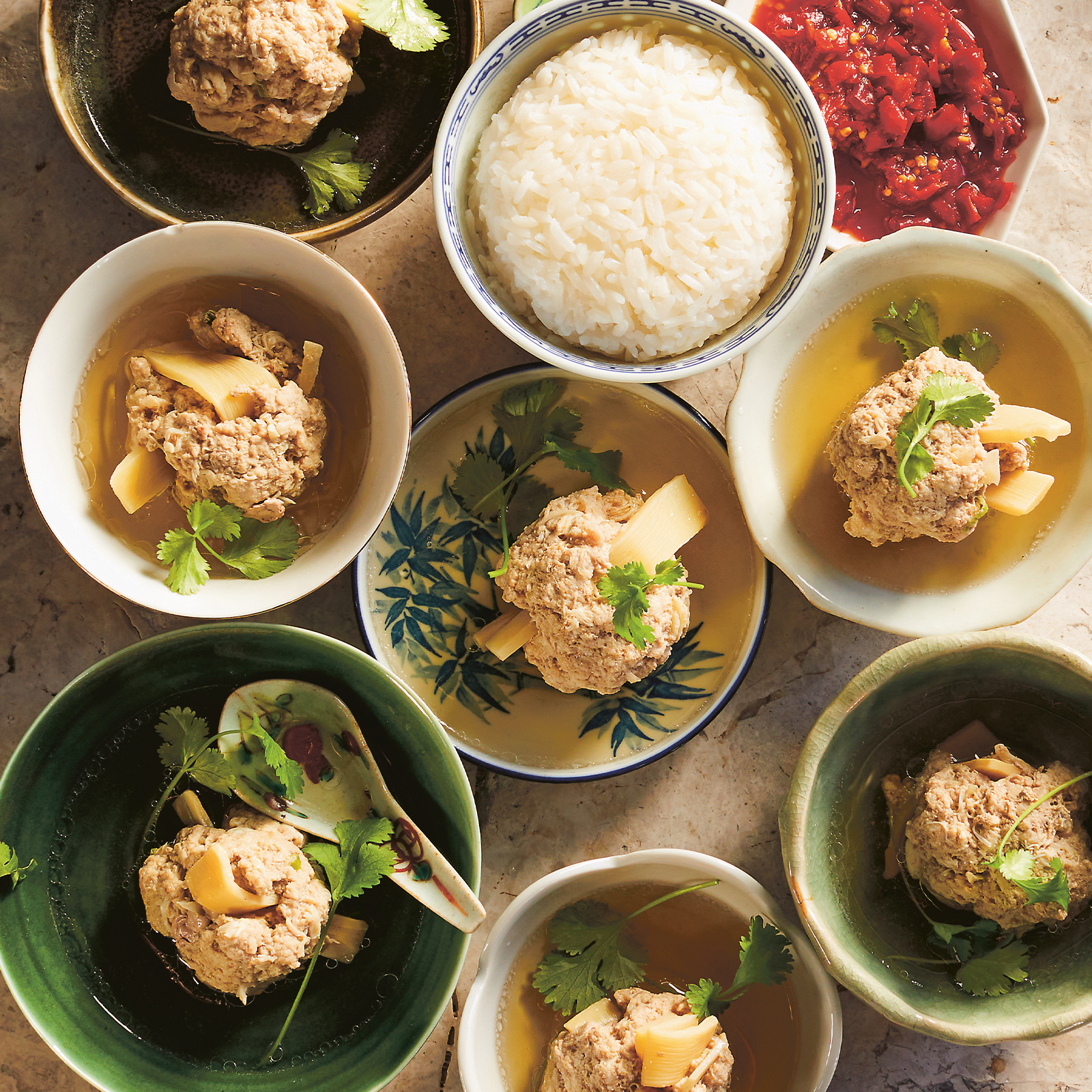 Lots of small bowls of gluten-free Nyonya Soup with pork and crab meatballs are arranged ready for serving with a small bowl of steamed rice and chilli.