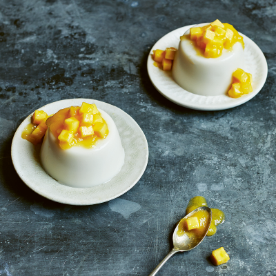 Two coconut panna cotta sitting on individual serving plates and topped with mango coulis.