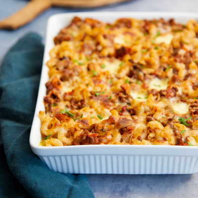 White baking dish with gluten-free cheesy pasta bake. A dark teal napkin rests on the side.