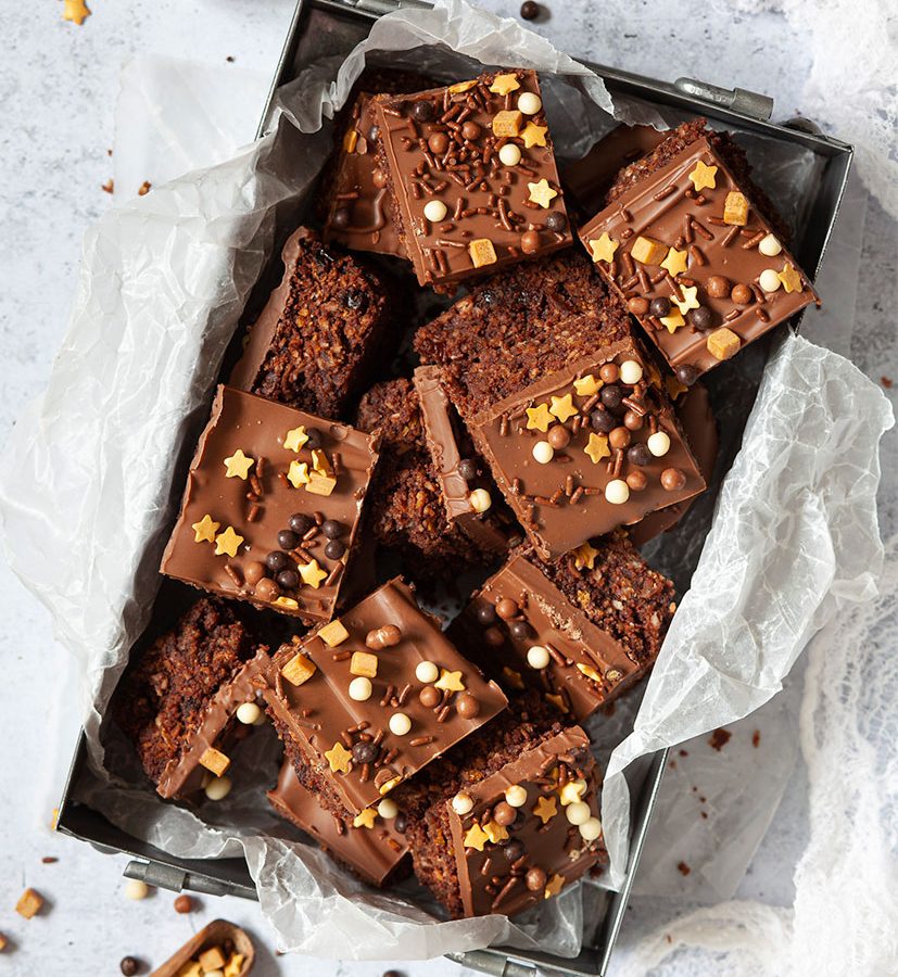 Chocolate crunch slice topped with gluten-free sprinkles. Cut into squares and arranged in a lined metal baking dish.