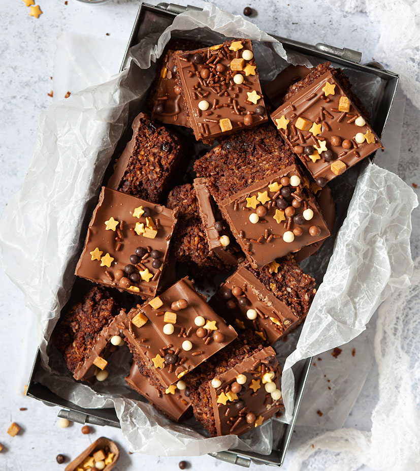 Chocolate crunch slice topped with gluten-free sprinkles. Cut into squares and arranged in a lined metal baking dish.