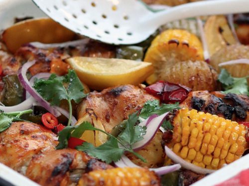 A gluten-free chicken tandoori tray bake with corn and onion in an enamel baking dish.