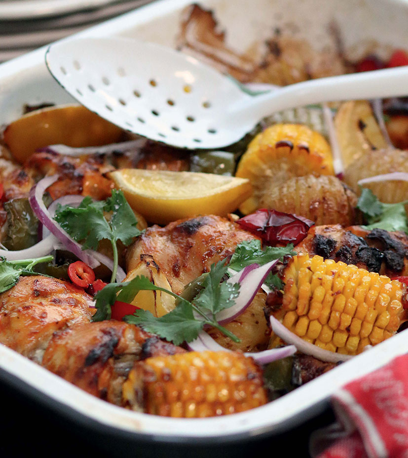 A gluten-free chicken tandoori tray bake with corn and onion in an enamel baking dish.